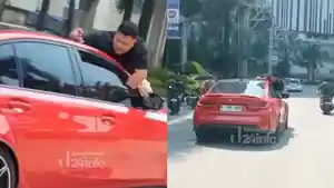 pria-nekat-bergelantung-diatas-sebuah-mobil-berwarna-merah.jpg