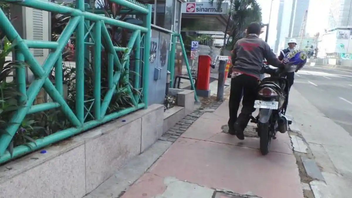 Di Jalan Thamrin Pria Ini Tidak Naik Sepeda Motor Tapi Mendorongnya