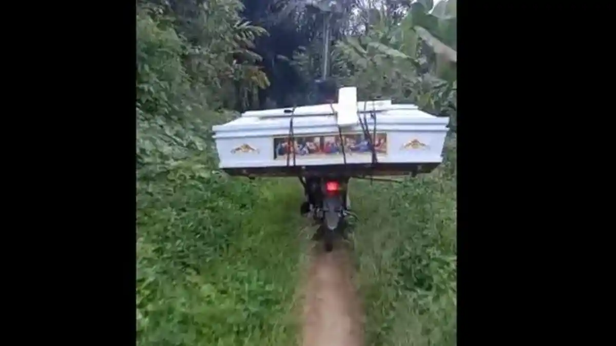 Seorang Pemotor Bawa Peti Mati Melewati Jalan Rusak