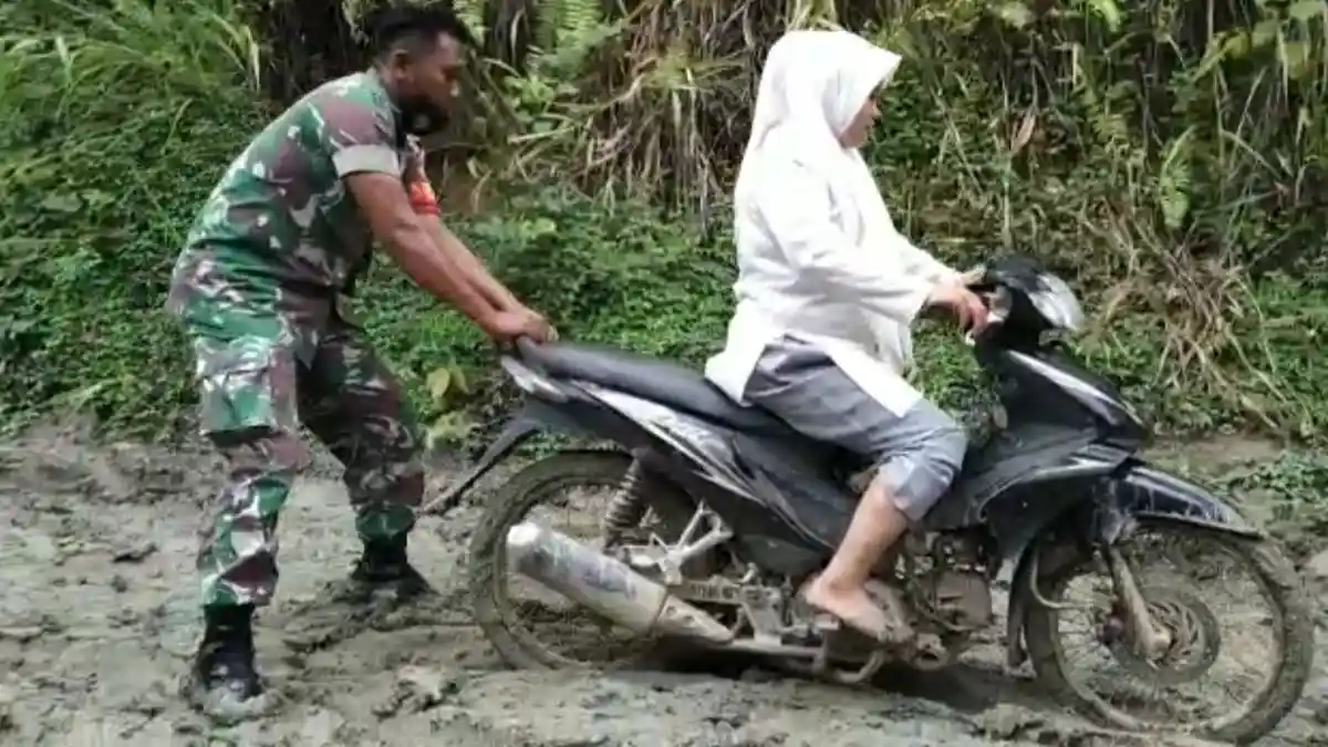 Babinsa Bantu Warga Lintasi Jalan Berlumpur di Birem Bayeun